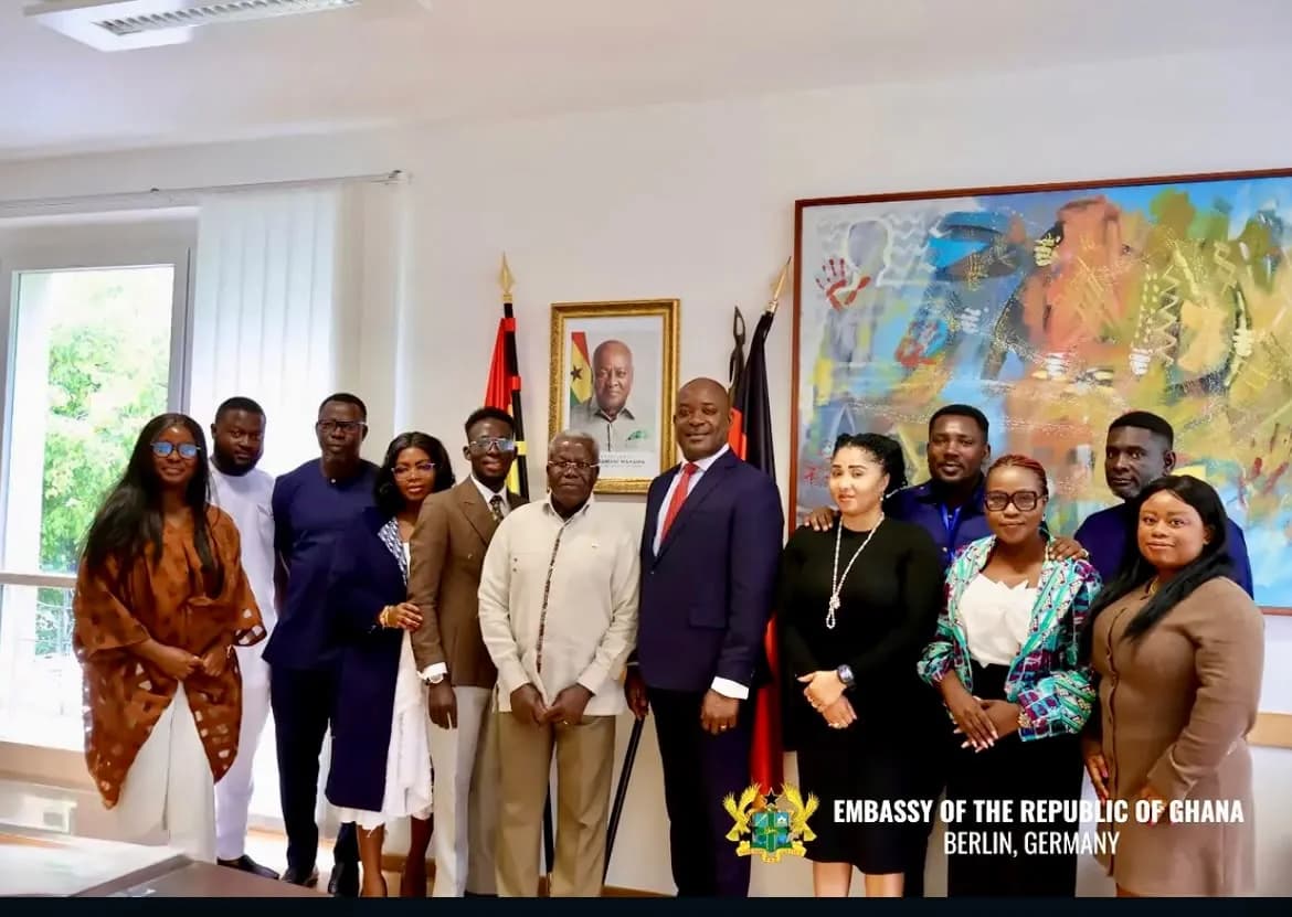 Delegation members posing together beside a Ghanaian flag.